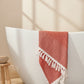 A green body towel with a herringbone pattern is draped over the edge of a bathtub, displaying its texture and color.