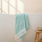 A green body towel with a herringbone pattern is draped over the edge of a bathtub, displaying its texture and color.